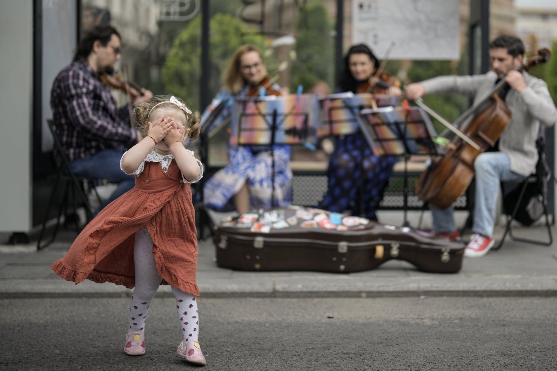 Малко момиченце покрива очите си, докато квартет изпълнява класическа музика на автобусна спирка в Букурещ, неделя, 29 май 2022 г.
