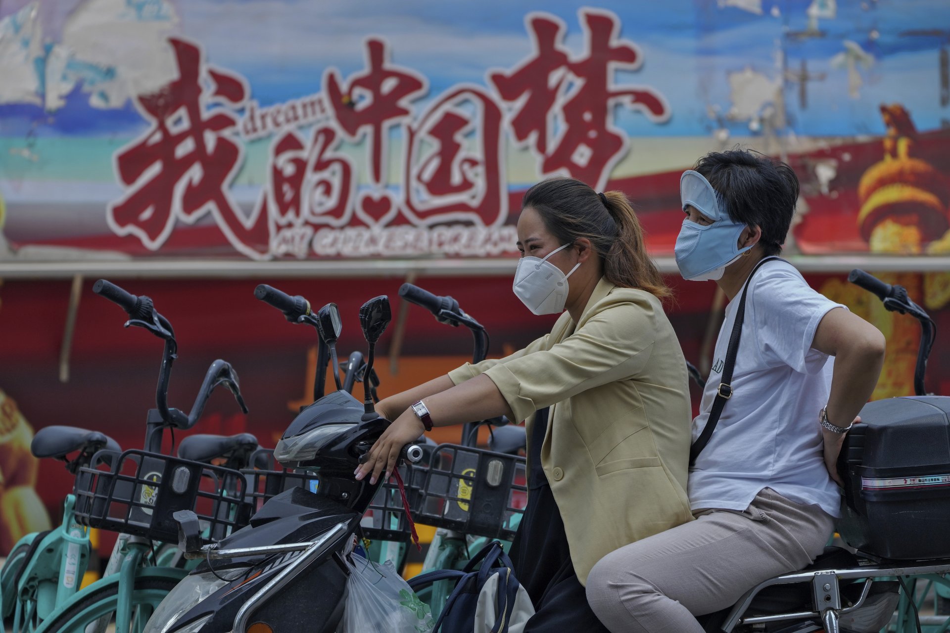 Жени с предпазни маски на скутер на фона на плакат, популяризиращ "китайската мечта", Пекин, понеделник, 20 юни 2022 г.