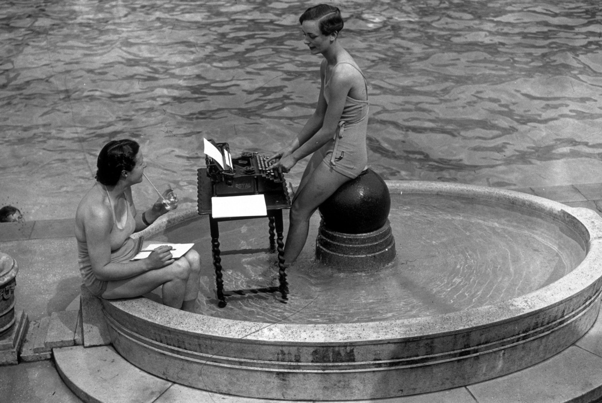 Около 1937 г.: Две градски машинописки на работа в открит плувен басейн през горещо лято. 