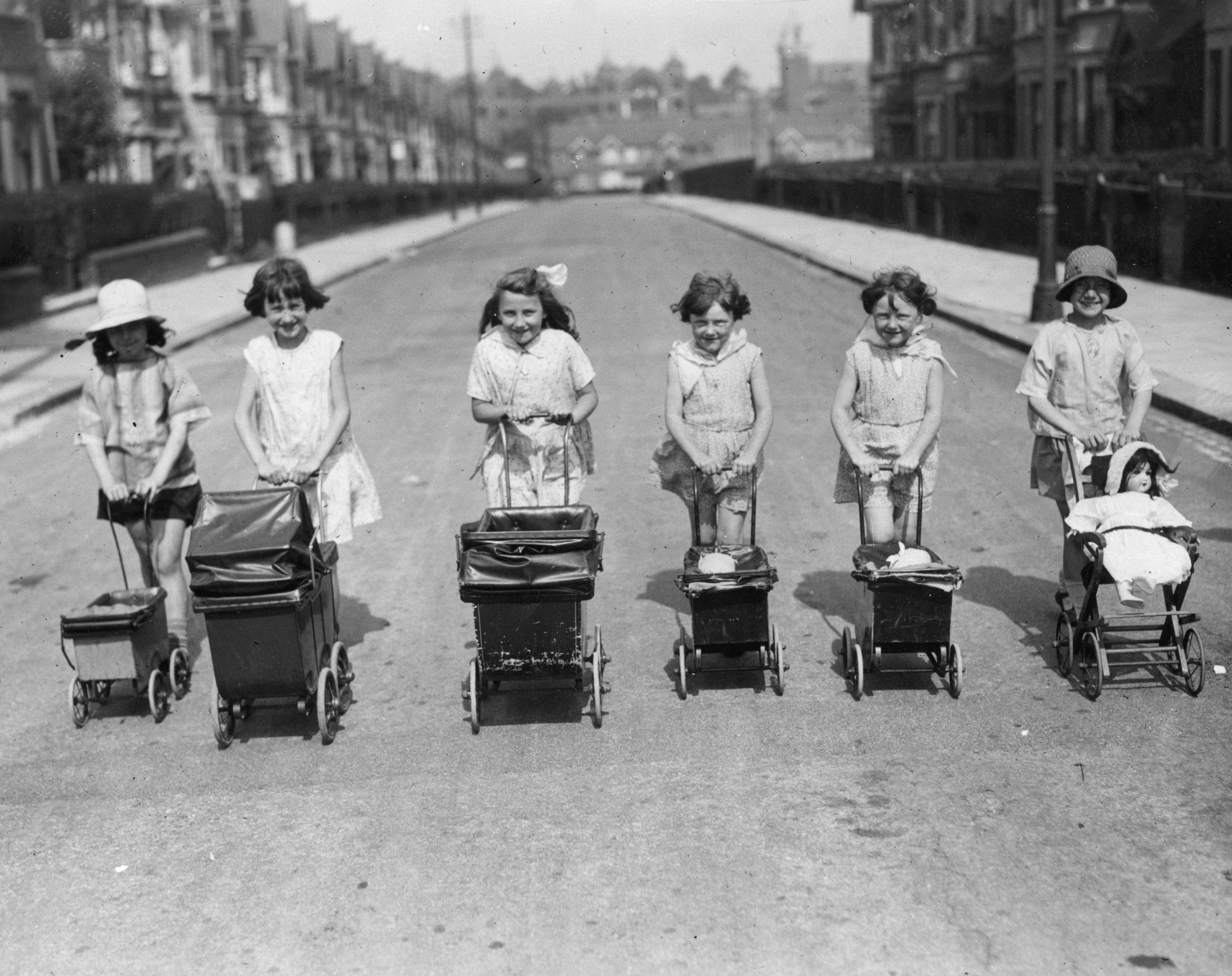 31 юли 1935 г.: Редица от щастливи малки момиченца, бутащи количките на своите кукли по улица по време на лятната ваканция. 
