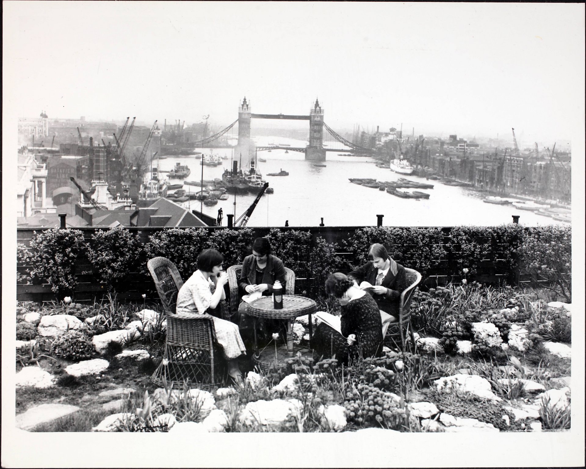 Градски момичета, наслаждаващи се на почивката си по време на обяд, в градината на покрива на Adelaide House, с изглед към басейна на Лондон и Тауър Бридж, Лондон, Англия, 25 май 1934 г. Великолепното лятно време, което се наблюдава в момента, изкарва работниците от града на открито за обедния им час. Тези щастливи служители нимат предимството на красива градина на покрива с изглед към Темза на Лондонския мост, където могат да се насладят на обяда си сред идеална среда. (Снимка от Fox Photos/Hulton Archive/Getty Images)