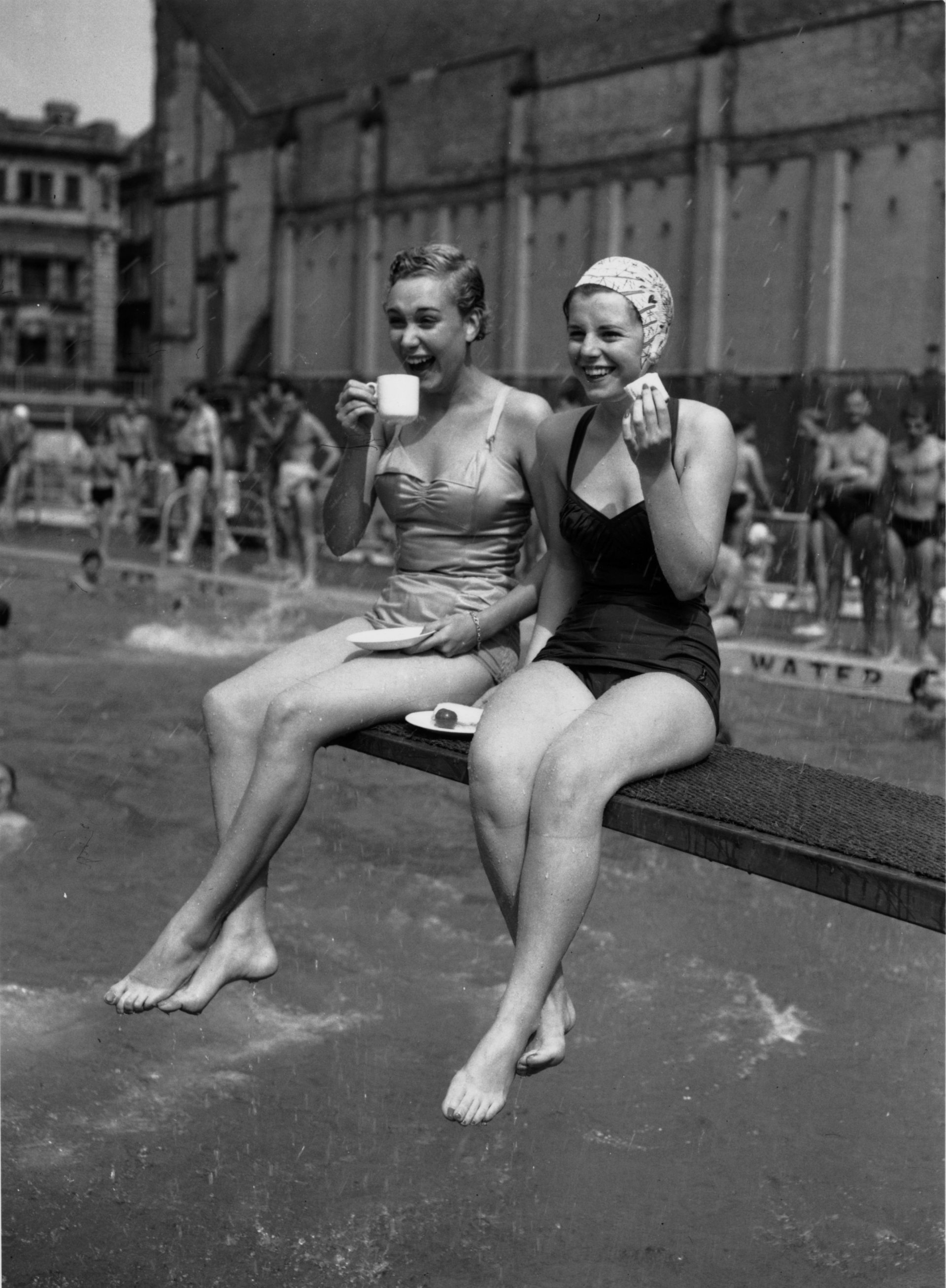 22 август 1955 г.: Офис служителки са избрали дъската за скачане в плувния басейн Holborn Oasis в Лондон като най-готиното място за обяд по време на горещата вълна. (Снимка от Monty Fresco Jnr/Topical Press Agency/Getty Images)