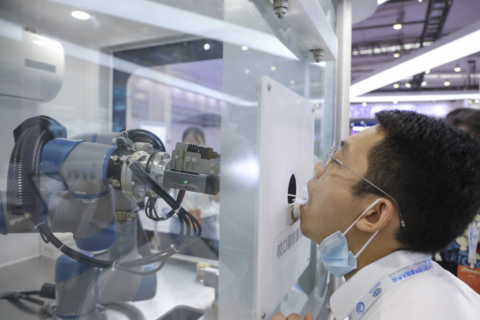 Член на персонала участва в демонстрация. Ръка на робот взима с тампони проба за COVID-19 по време на Световната конференция за роботи през 2022 г. 