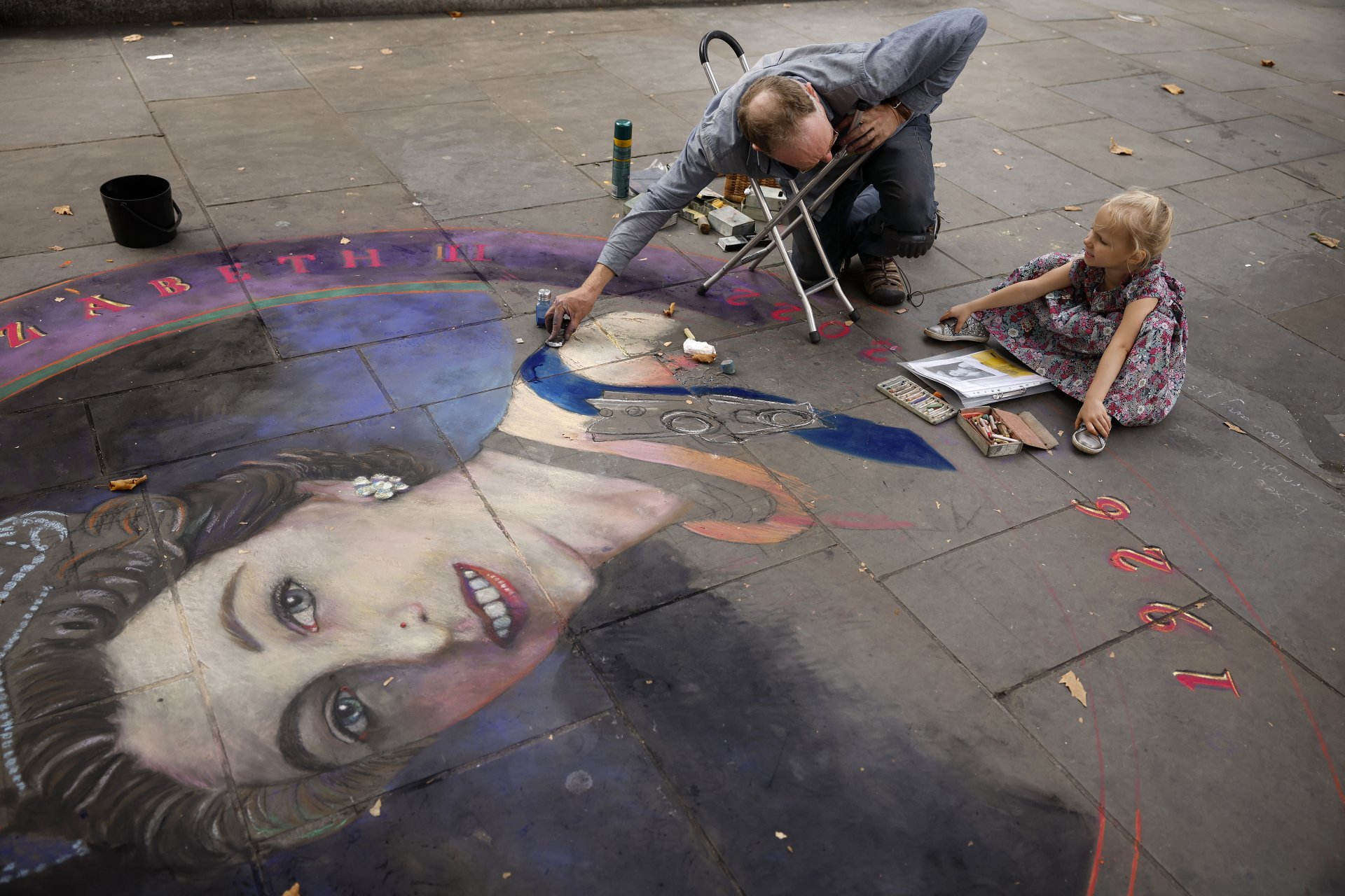 Тригодишната Вайълет Уилямс наблюдава как художникът Джулиан Бивър работи върху портрет на кралица Елизабет II, наарисуван с тебешири, на тротоара близо до площад Трафалгар.