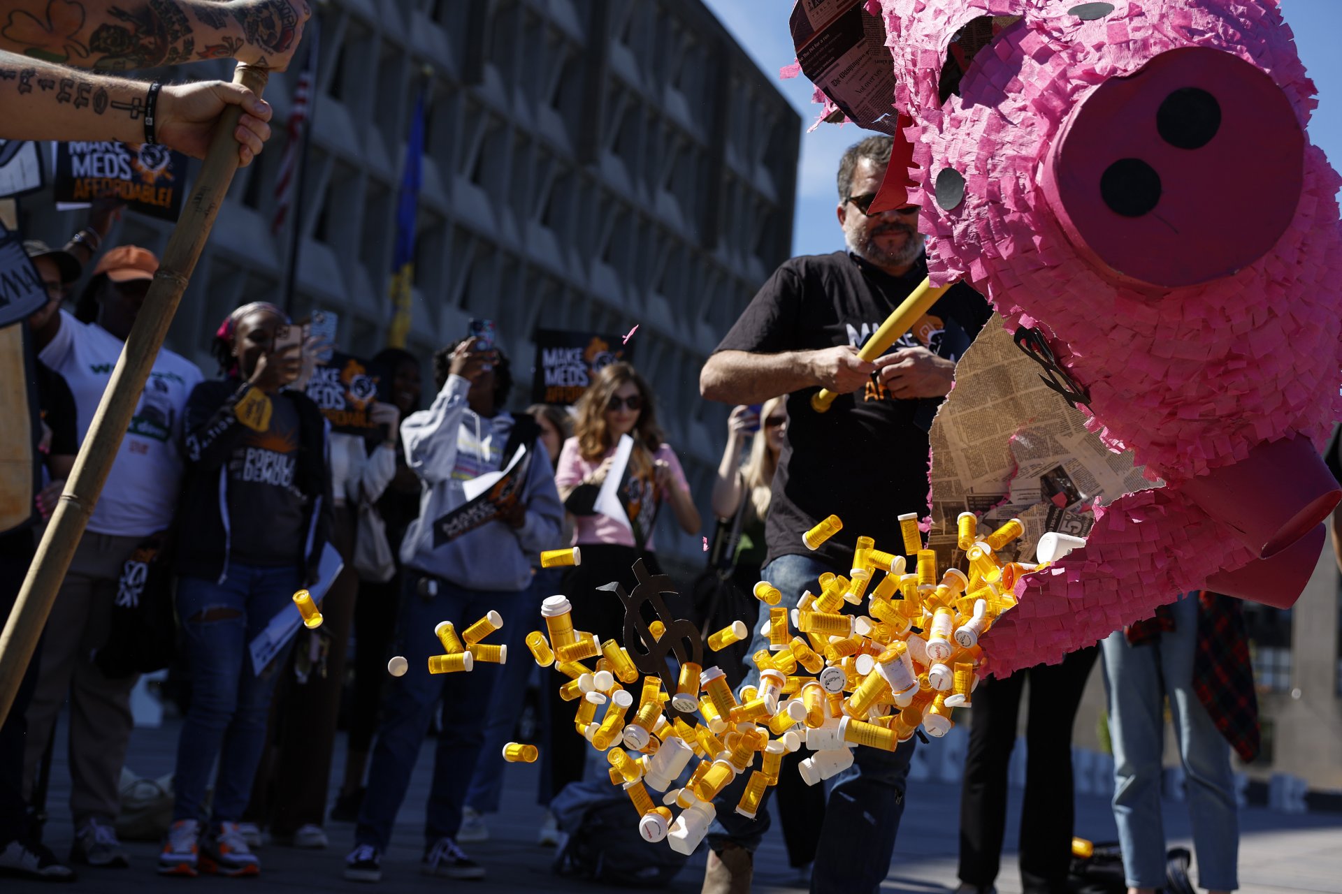Активисти удрят пинята, носеща празни бутилки от хапчета по време на протест срещу цената на лекарстваta, отпускани с рецепта, пред сградата на Министерството на здравеопазването и човешките услуги в САЩ
