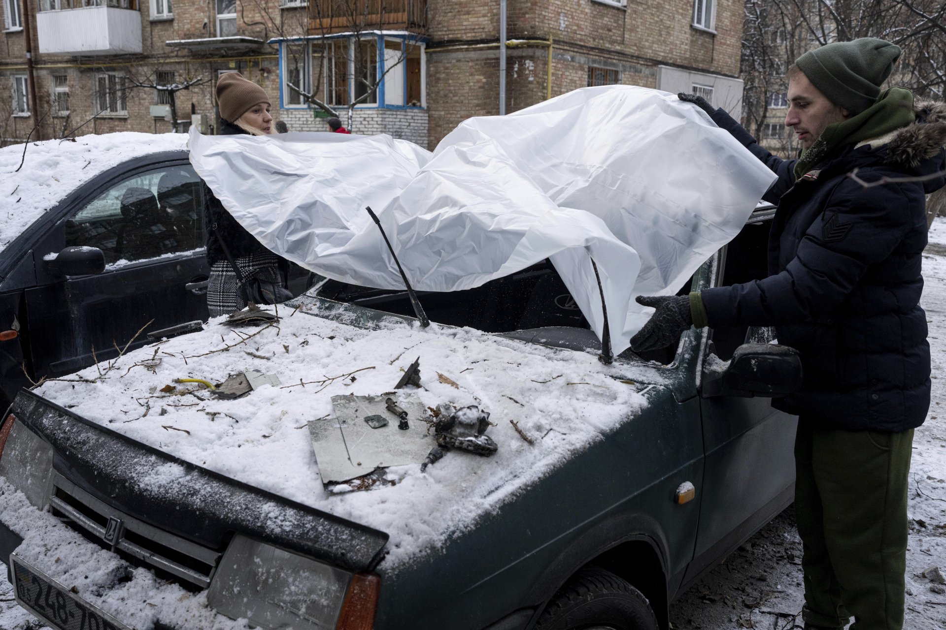 Двойка покрива повредената си кола с пластмасов брезент след руска атака в Киев