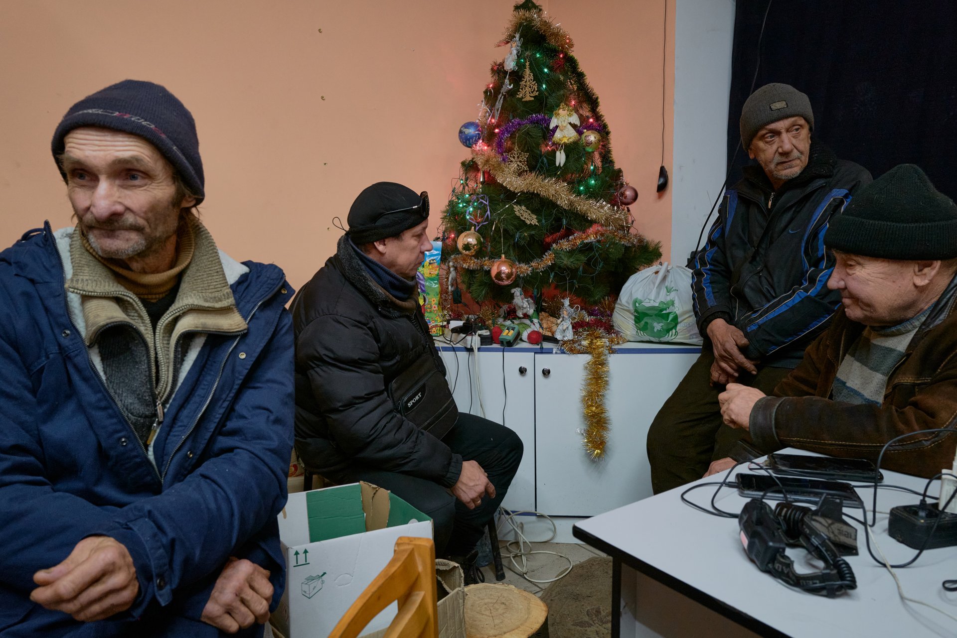 Местните жители зареждат телефоните си близо до коледна елха в хуманитарен център на фона на артилерийски обстрел на 24 декември 2022 г. в Бахмут, Украйна.