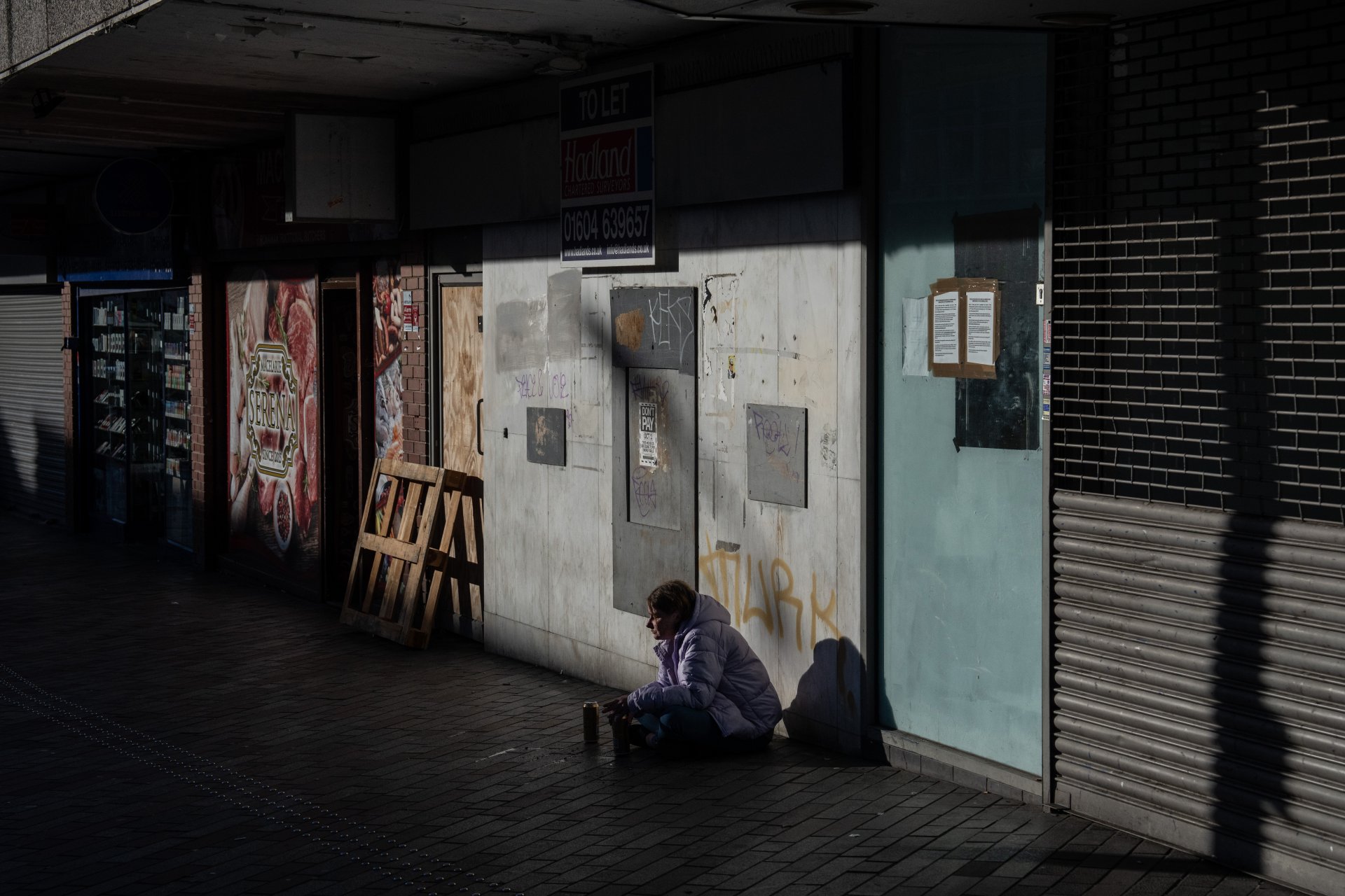 Бездомна жена проси пред заковани с дъски магазини в града. Над 17 000 магазина на High Street затвориха завинаги в Обединеното кралство през 2022 г. 