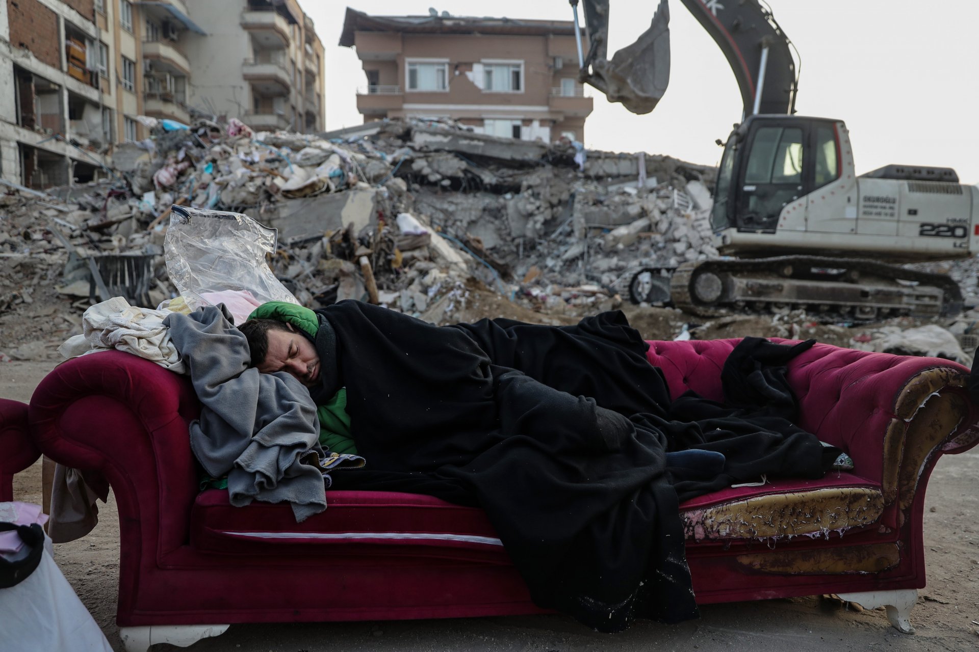 Мъж спи на диван близо до срутена сграда на 13 февруари 2023 г. в Хатай, Турция. 