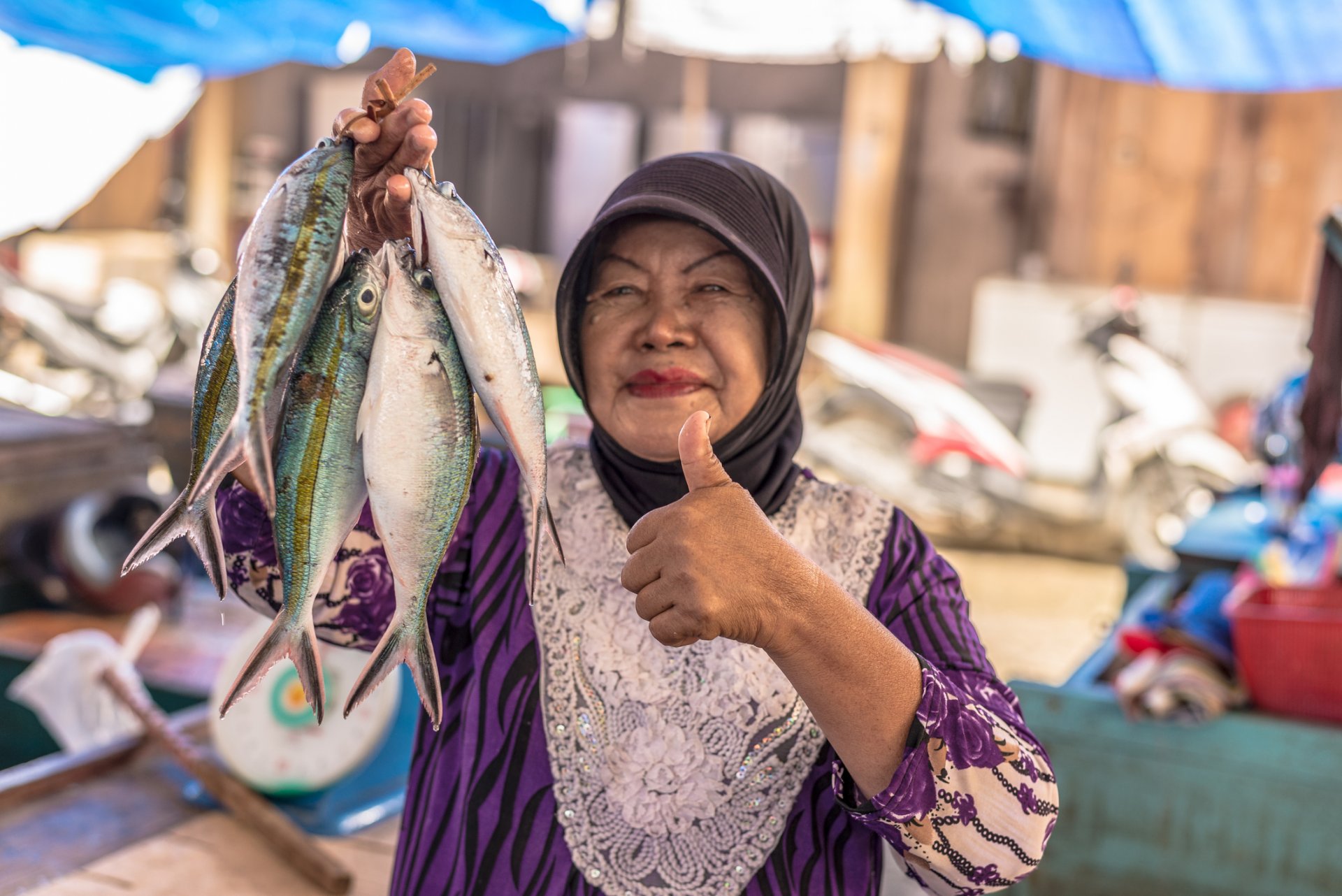 Индонезийка в традиционна носия държи връзка с риба, която предлага на местен пазар