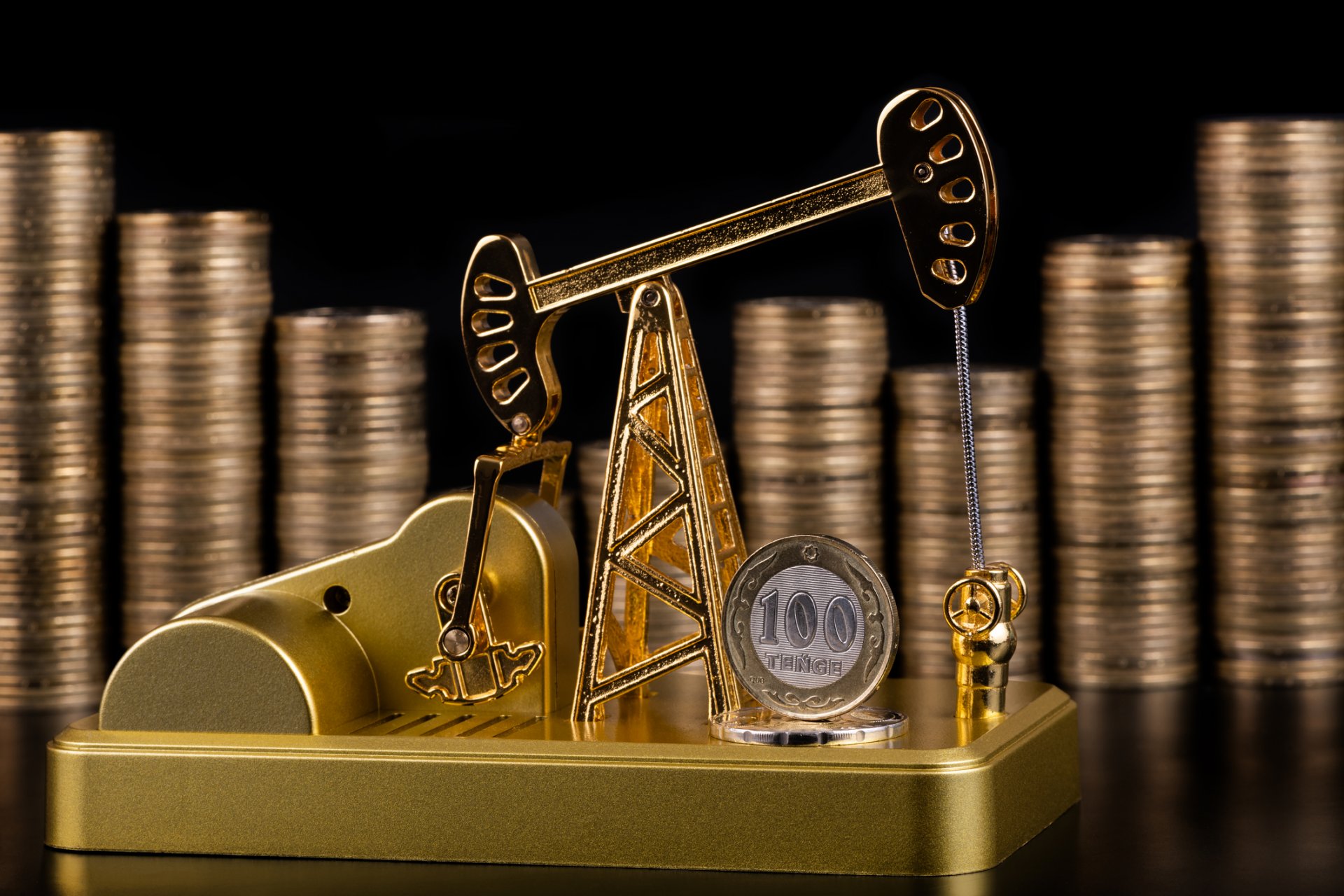Илюстративно изображение на добив на петрол със златна сонда на фона на струпани в колони казахстански монети от по 100 тенге