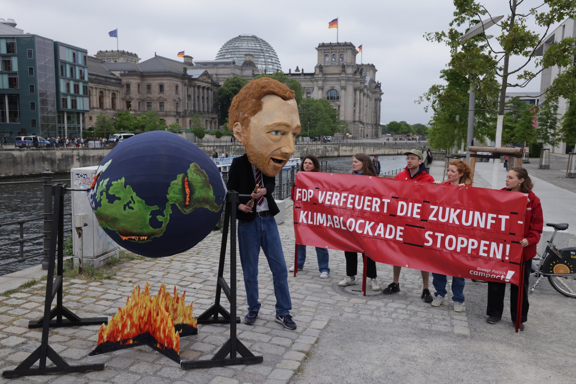 Активист, облечен като германския министър на финансите и лидер на Германските свободни демократи (FDP) Кристиан Линднер, върти глобус върху симулативен огън, докато други активисти държат банер, който гласи: "FDP изгаря бъдещето - спрете климатичната блокада!" близо до Райхстага на 23 май 2023 г. в Берлин, Германия. 
