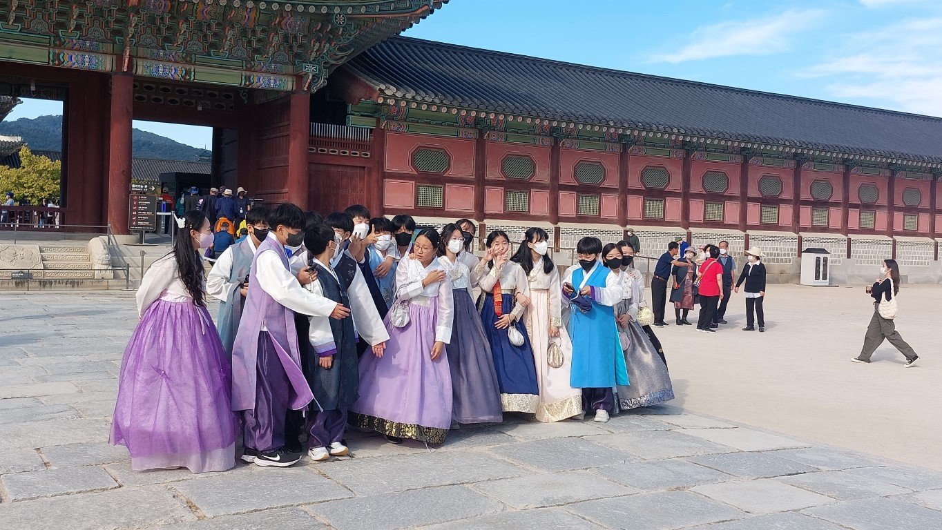 Един от дворците на Сеул с групи младежи, облечени в ханбок