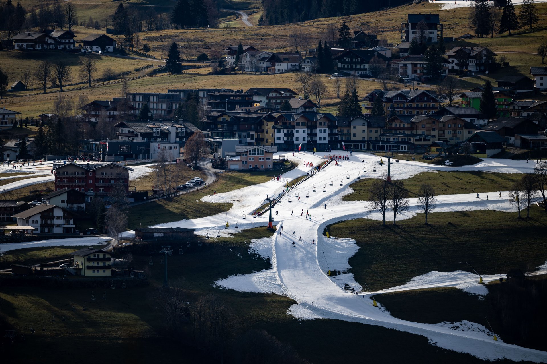  Скиори се спускат по склоновете на зоната Rohrmoos, покрита с изкуствен сняг. Тревата се вижда по останалата част от хълма. Алпийските ски курорти в Австрия, Германия и Швейцария бяха изправени пред необичайно топъл януари, на фона на рекордните температури и в други части на Европа. 