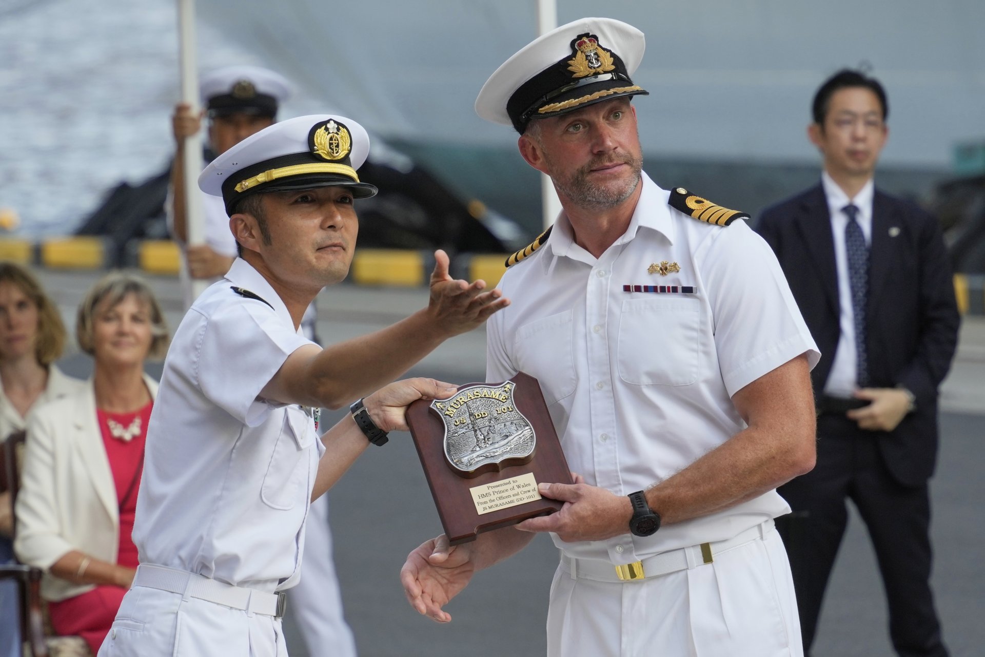 Капитан Уил Блекет, вдясно, командир на самолетоносача на Кралския флот HMS Prince of Wales (R09), разменя подаръци с командир Масахиро Хаякава, командир на разрушителя JS Murasame (DD-101) на Японските морски сили за самоотбрана, по време на церемонията