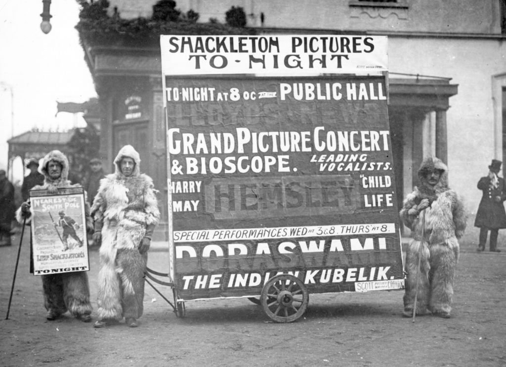 Мъже, облечени в кожи на арктически изследователи, рекламират лекцията на сър Ърнест Шакълтън за неговите експедиции до Антарктида и Южния полюс.