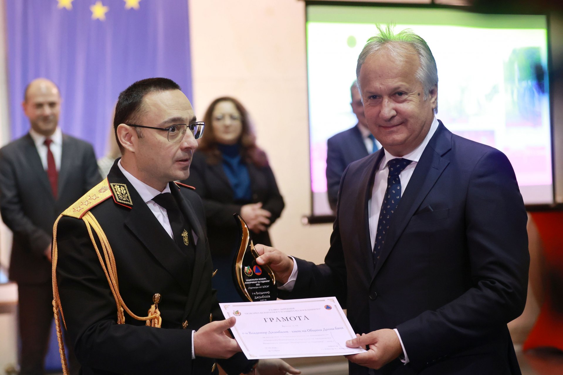 На снимката: директорът на ГДПБЗН главен комисар Александър Джартов (вляво) връчва отличие на кмета на община Долна баня Владимир Джамбазов