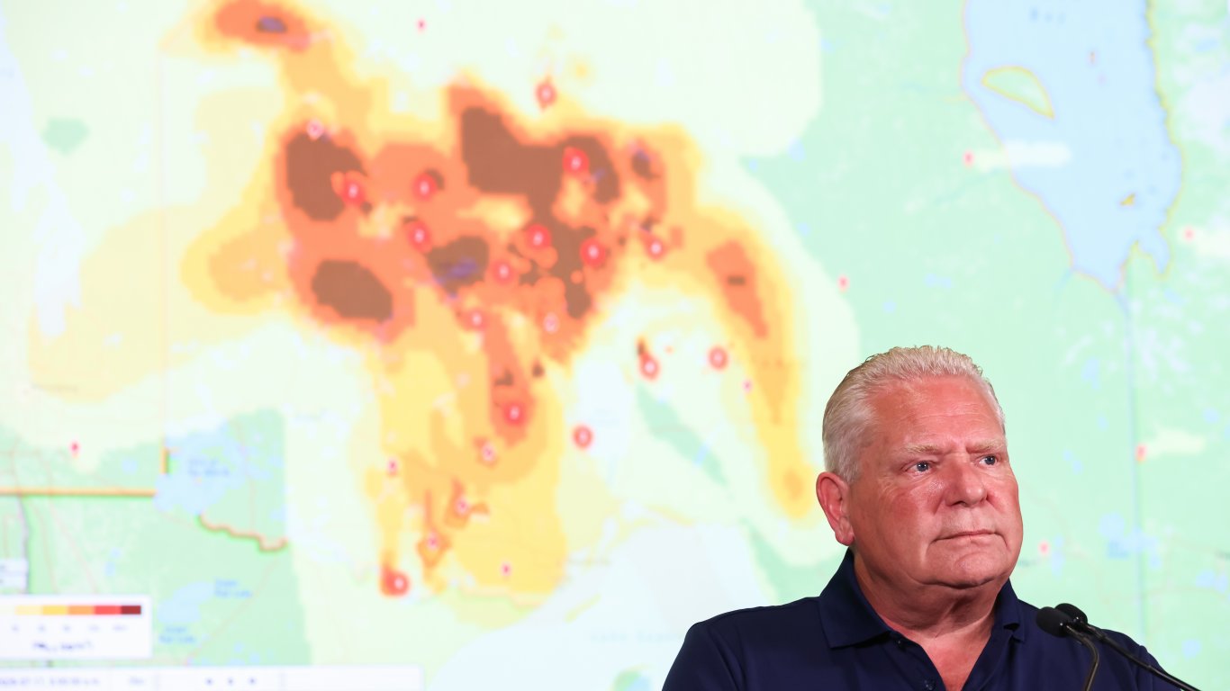 Премиерът на канадската провинция Онтарио Дъг Форд на фона на карта, която в реално време показва движението на дима от горските пожари в Канада